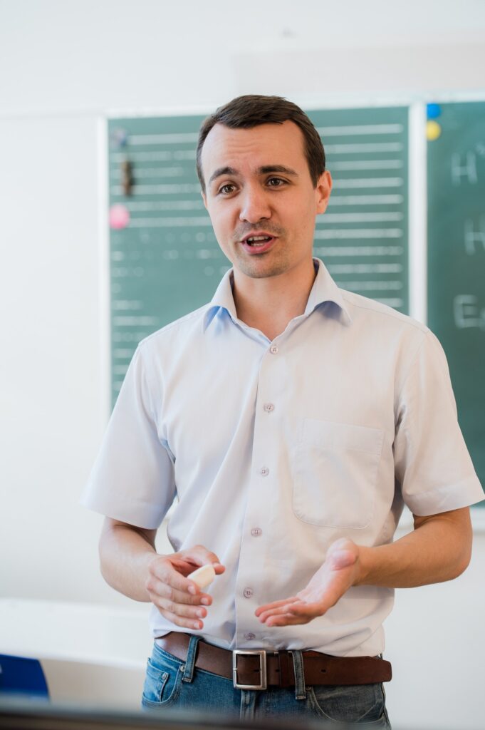 young teacher near chalkboard in school classroom talking to class